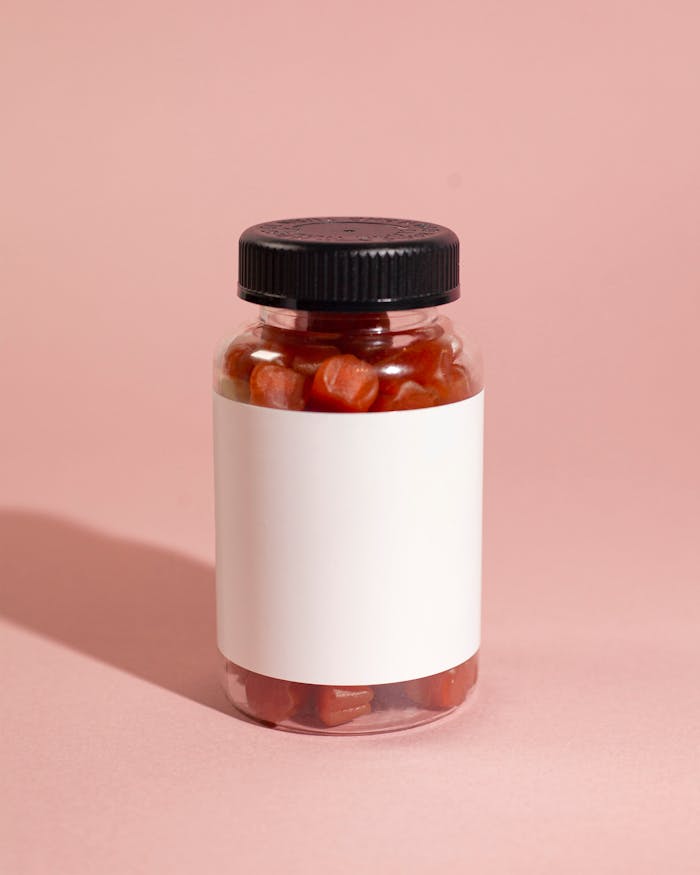 A clear bottle of gummy vitamins with a blank label on a pink background.