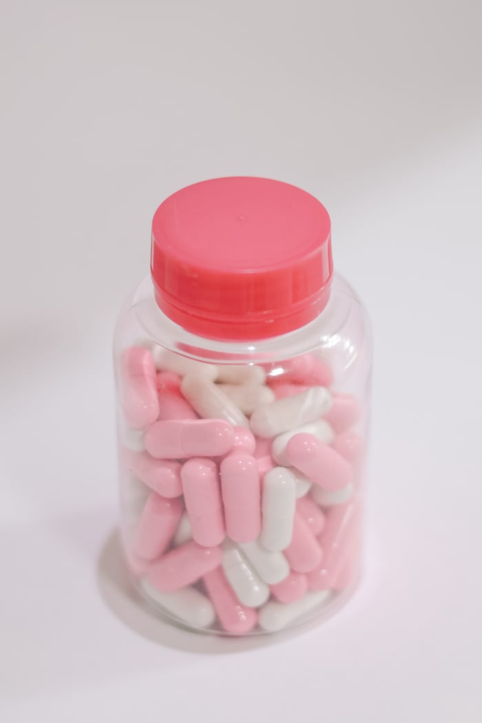 A clear bottle filled with pink and white capsules, captured on a neutral background.