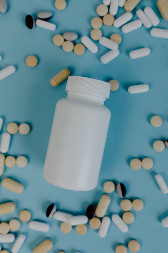 Closeup of a white bottle surrounded by various pills on a blue surface.